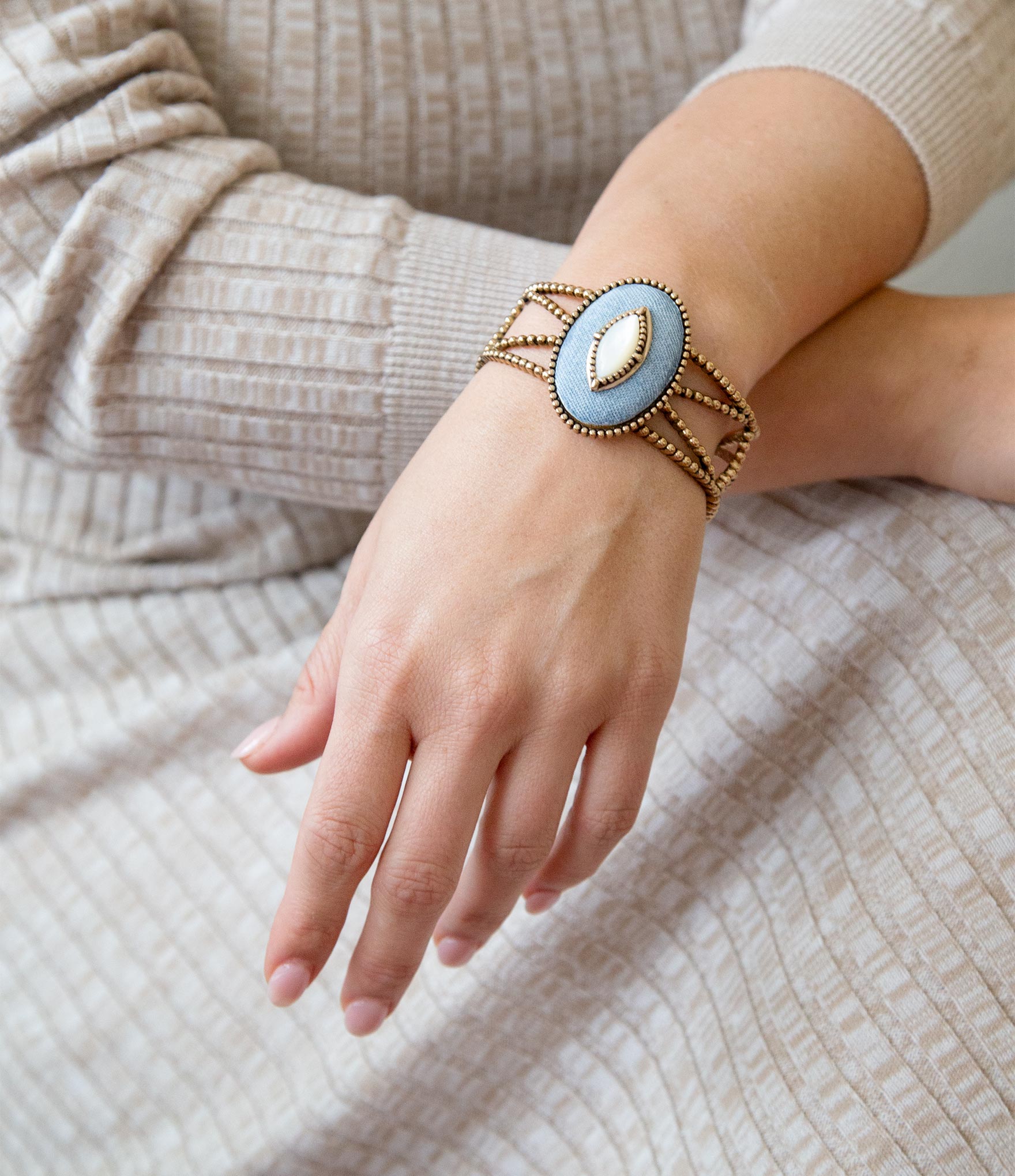 Hand wearing a gold bracelet with a blue stone on a neutral background