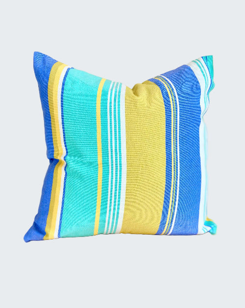 Striped pillow with blue, yellow, and white colors on a wooden stool against a beige wall.