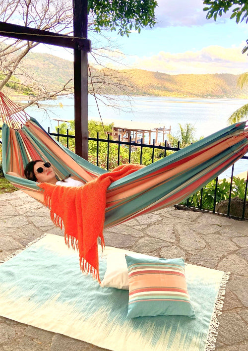 Person relaxing in a colorful hammock with a scenic view of water and mountains.