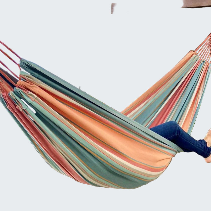 Person relaxing in a colorful striped hammock by a body of water with mountains in the background.