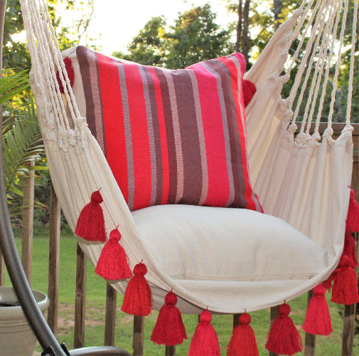 Beige hammock chair with red and brown striped pillow and tassels in an outdoor setting.