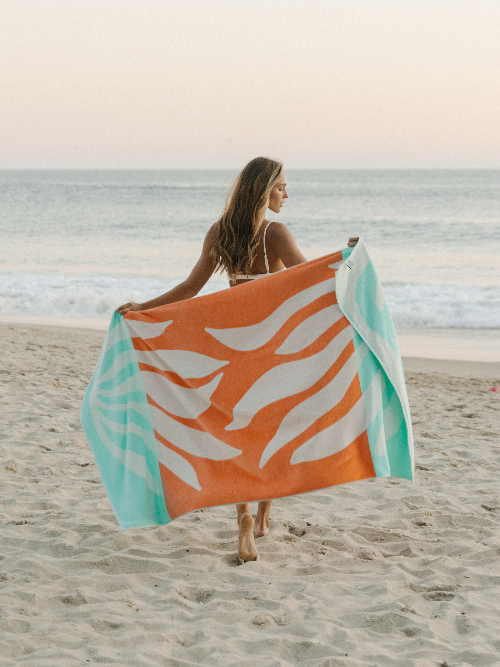 Woman holding a colorful beach towel on a sandy beach with ocean in the background
