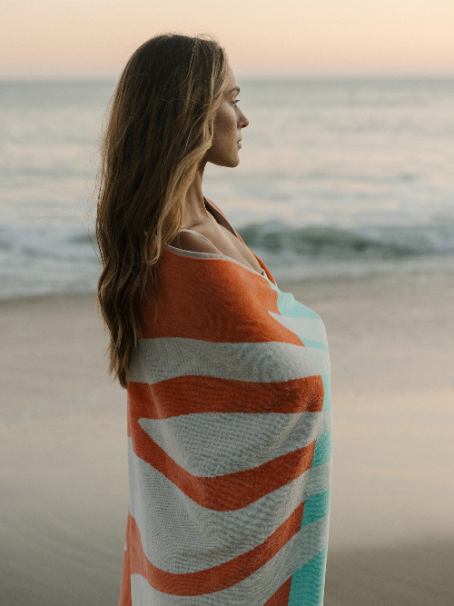 Woman wrapped in a colorful towel on a beach at sunset
