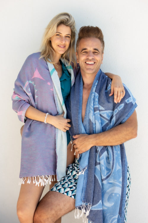 Two people wearing patterned towels against a white background