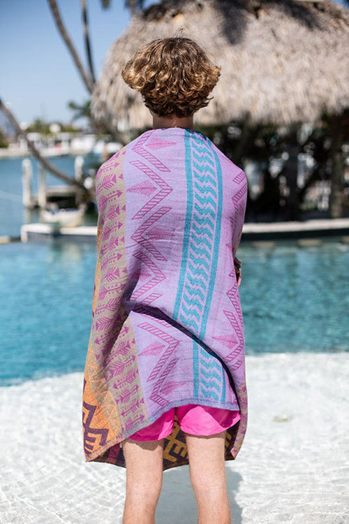 Person wearing a colorful towel with a geometric pattern by a waterfront.