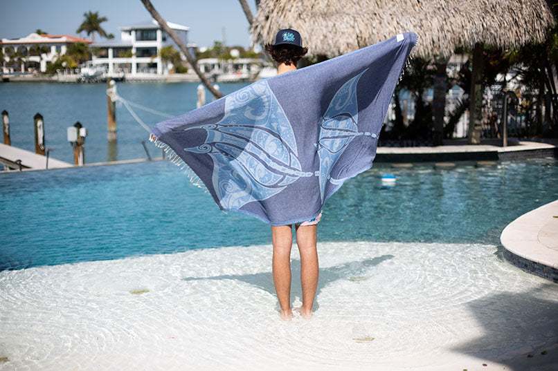 Person holding a blue towel by a poolside with a thatched-roof structure in the background.