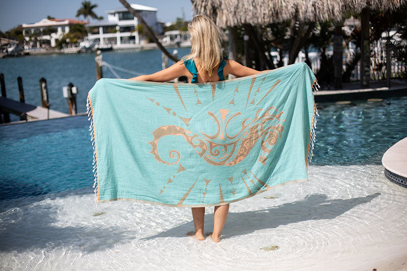 Person holding a turquoise towel with a gold design by a poolside.