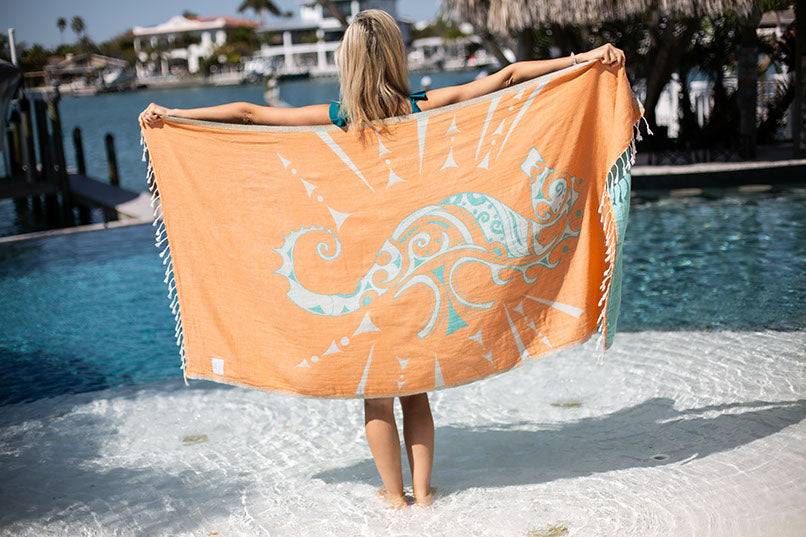 Person holding a large orange towel with a design by a pool