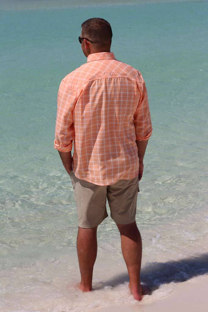Man in an orange checkered shirt and beige shorts standing in clear blue water.