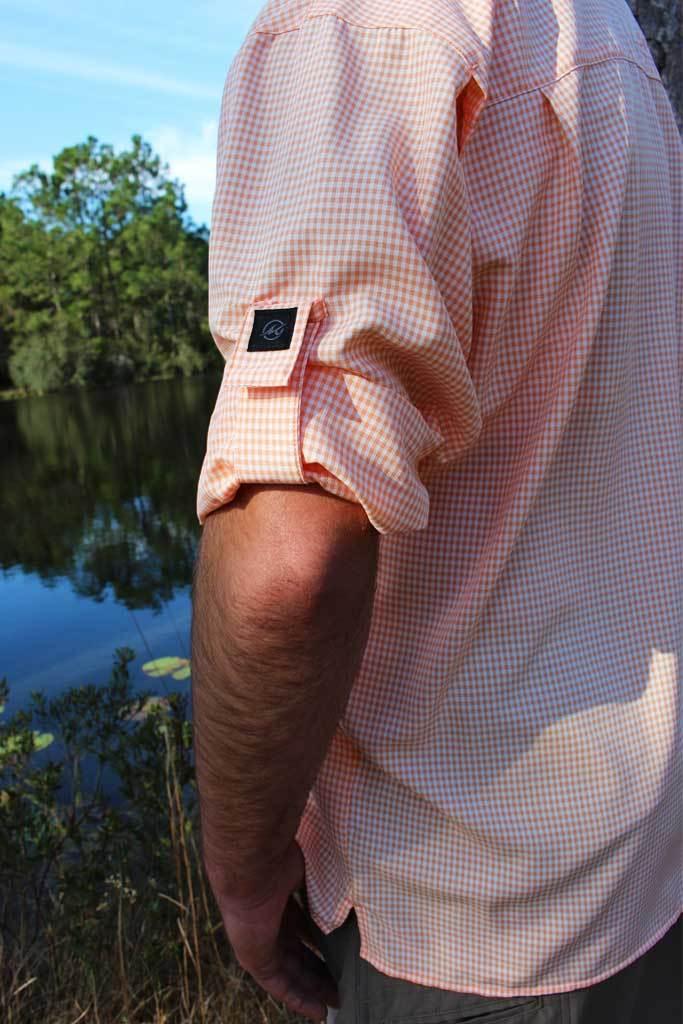 Person wearing a pink checkered shirt with a camera mounted on their chest, standing by a body of water.