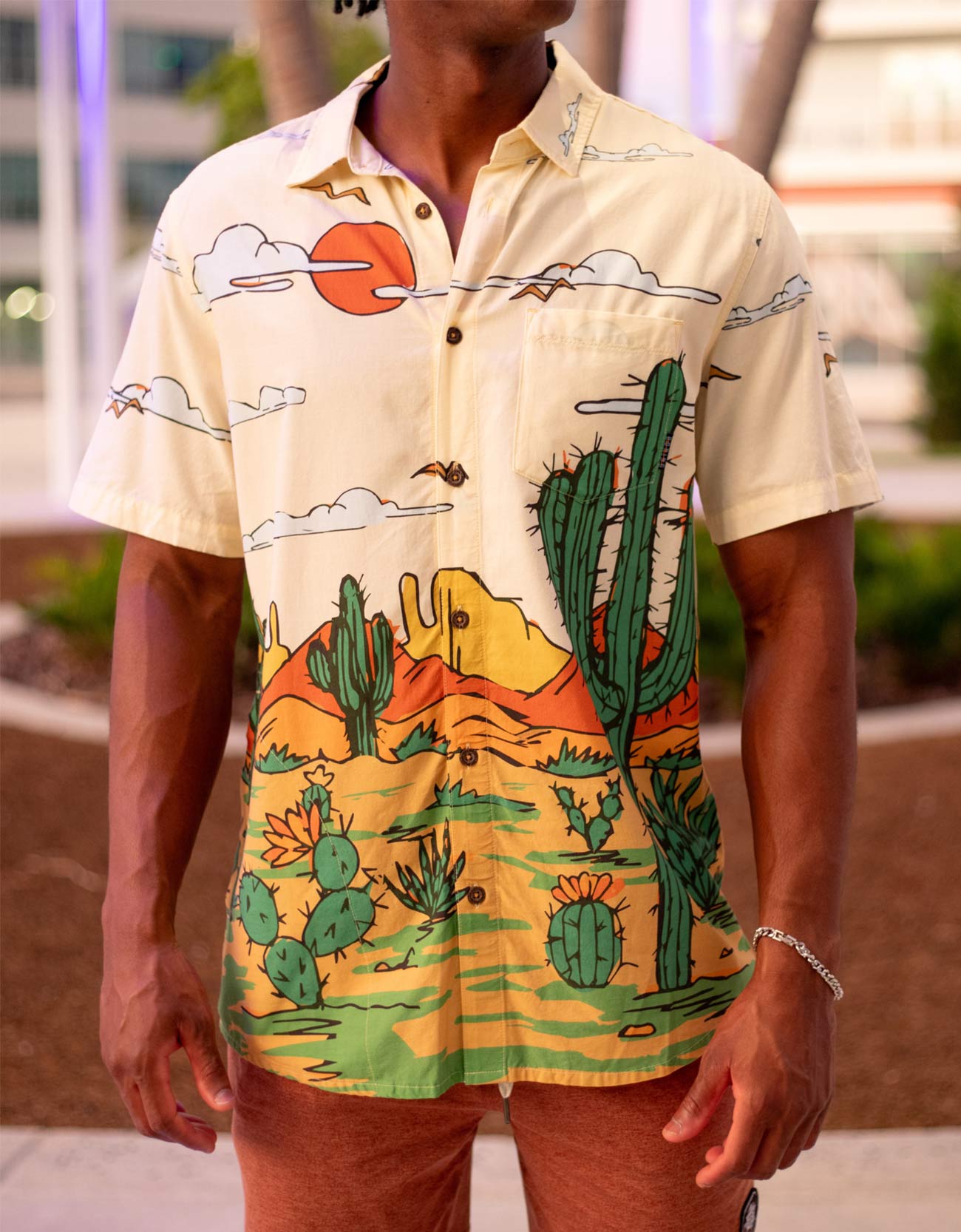 Person wearing a colorful shirt with desert-themed graphics outdoors.