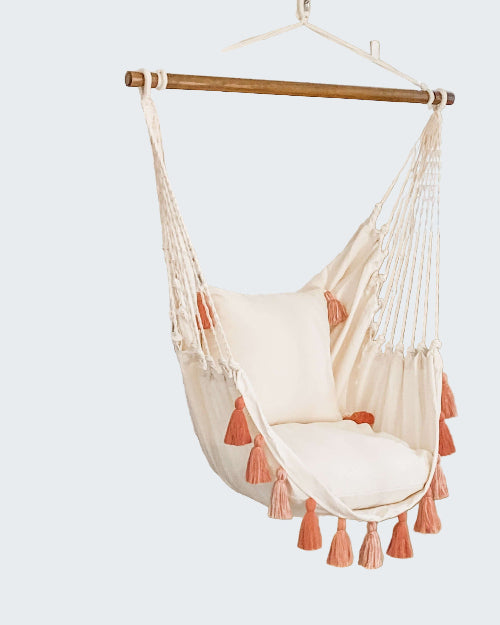 White hammock chair with pink tassels hanging in a room with a decorative screen and plant.