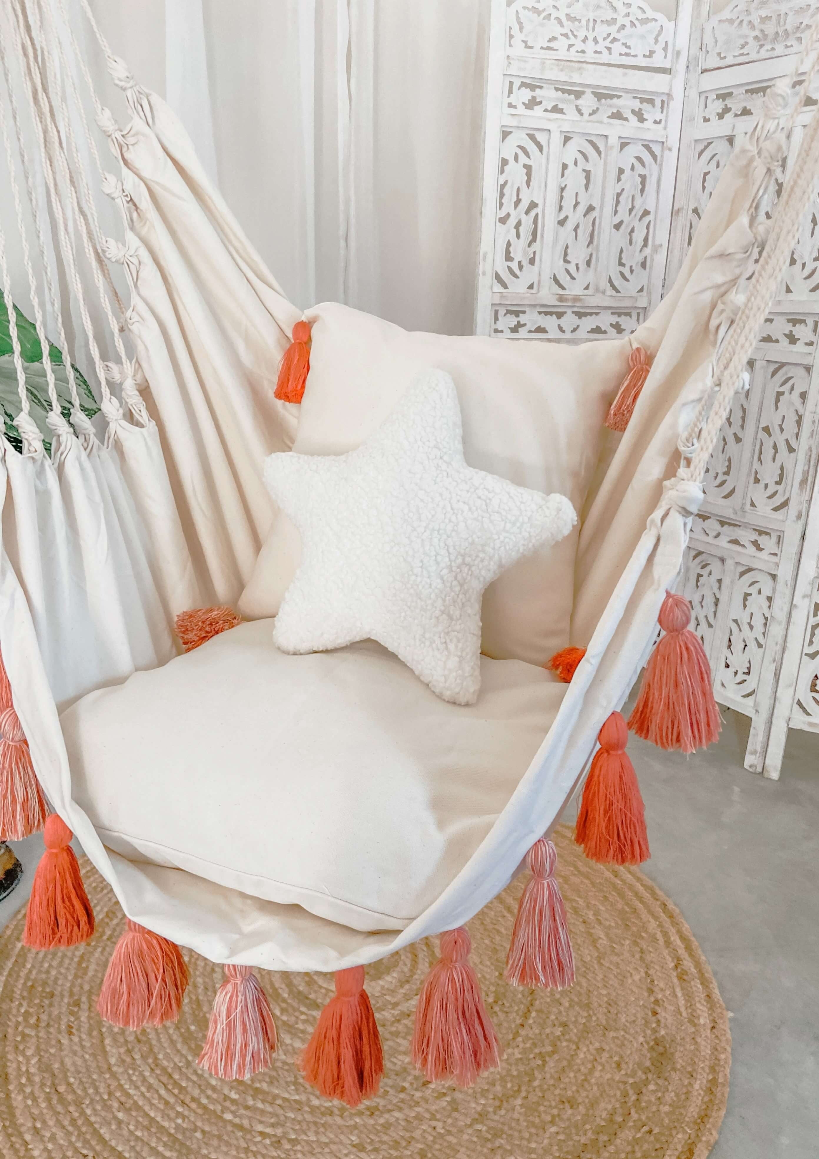 Hanging chair with white cushions and pink tassels in a decorative room.