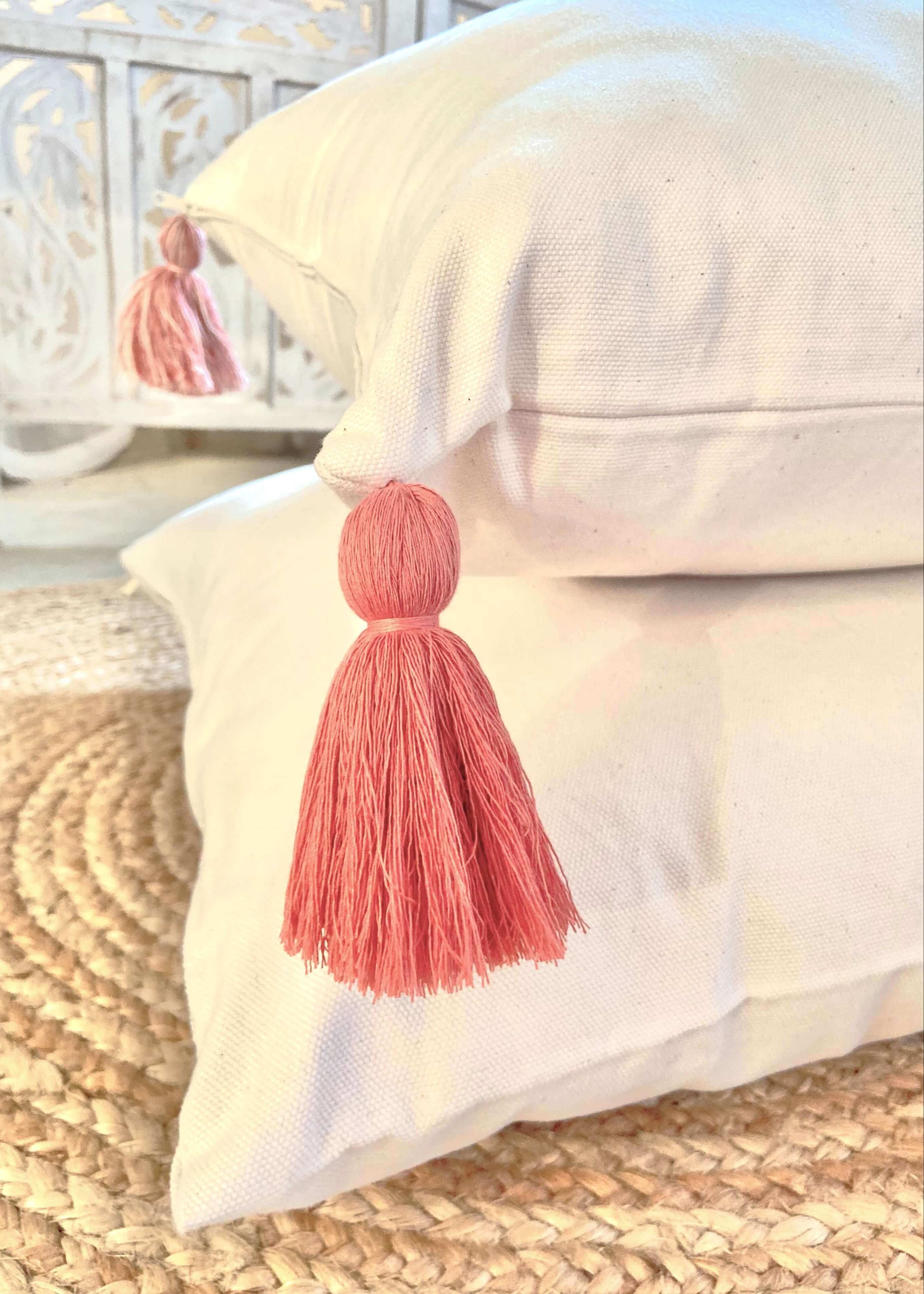 White pillows with pink tassels on a woven surface
