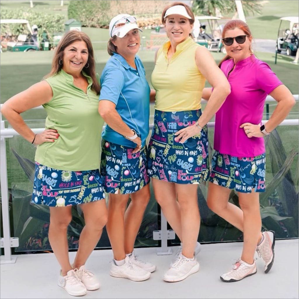 Four women posing together on a golf course wearing colorful outfits and patterned skirts.