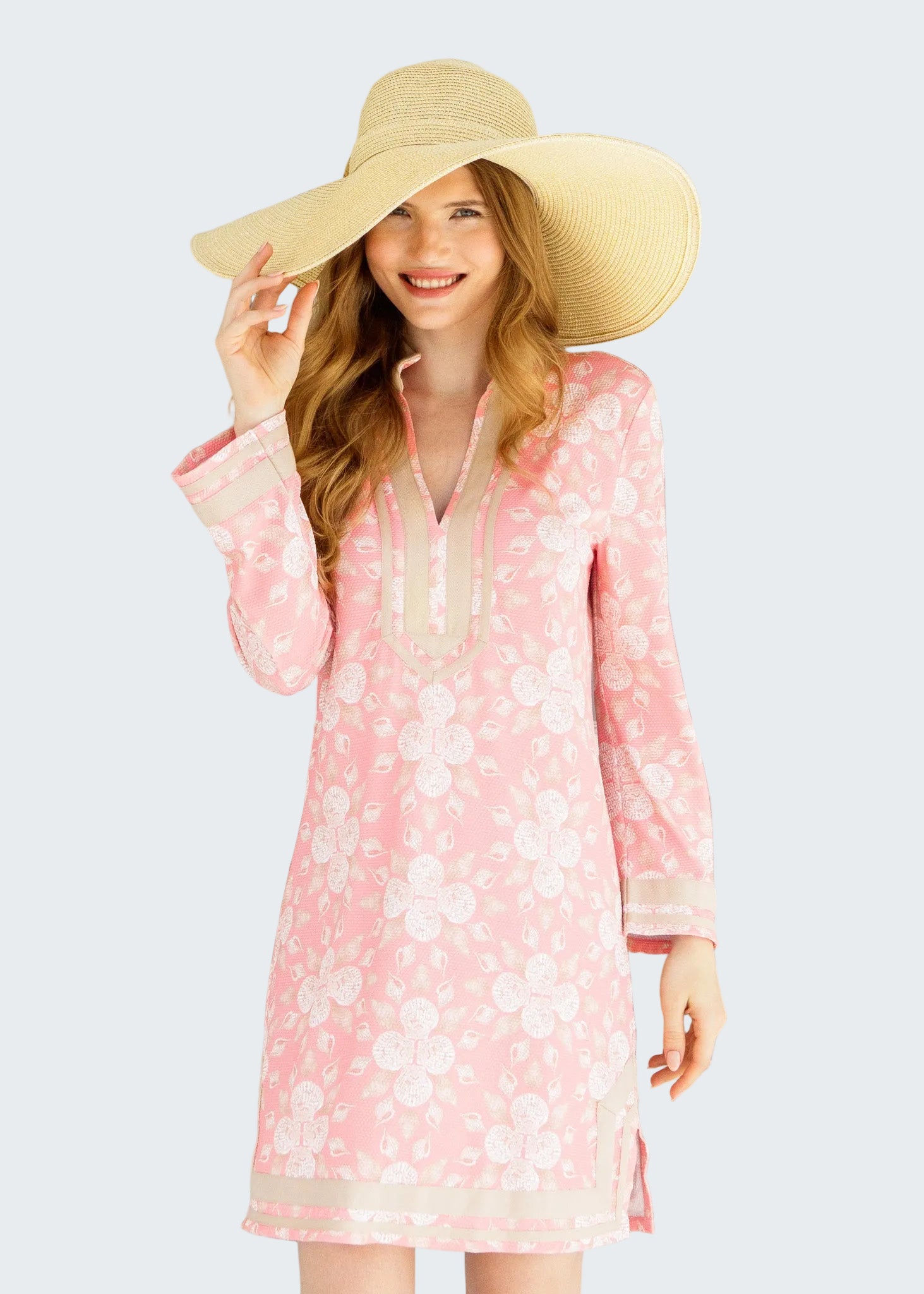 Woman wearing a pink floral dress and beige hat in front of a glass door.