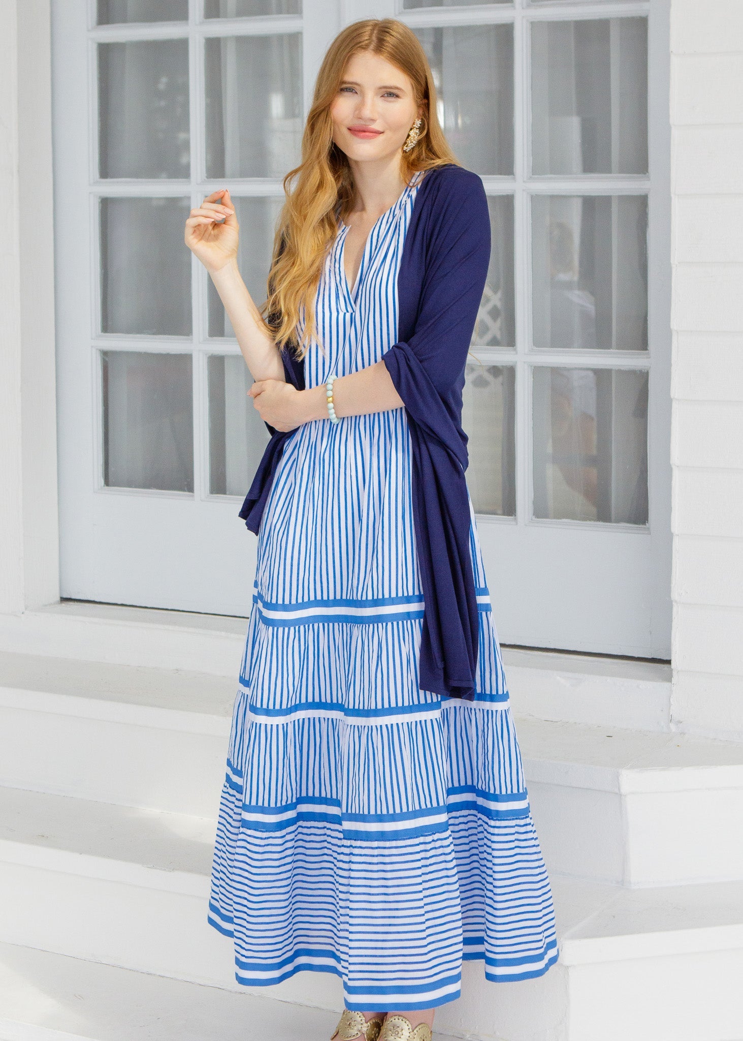 Woman wearing a blue and white striped dress with a matching cardigan in front of a glass door.