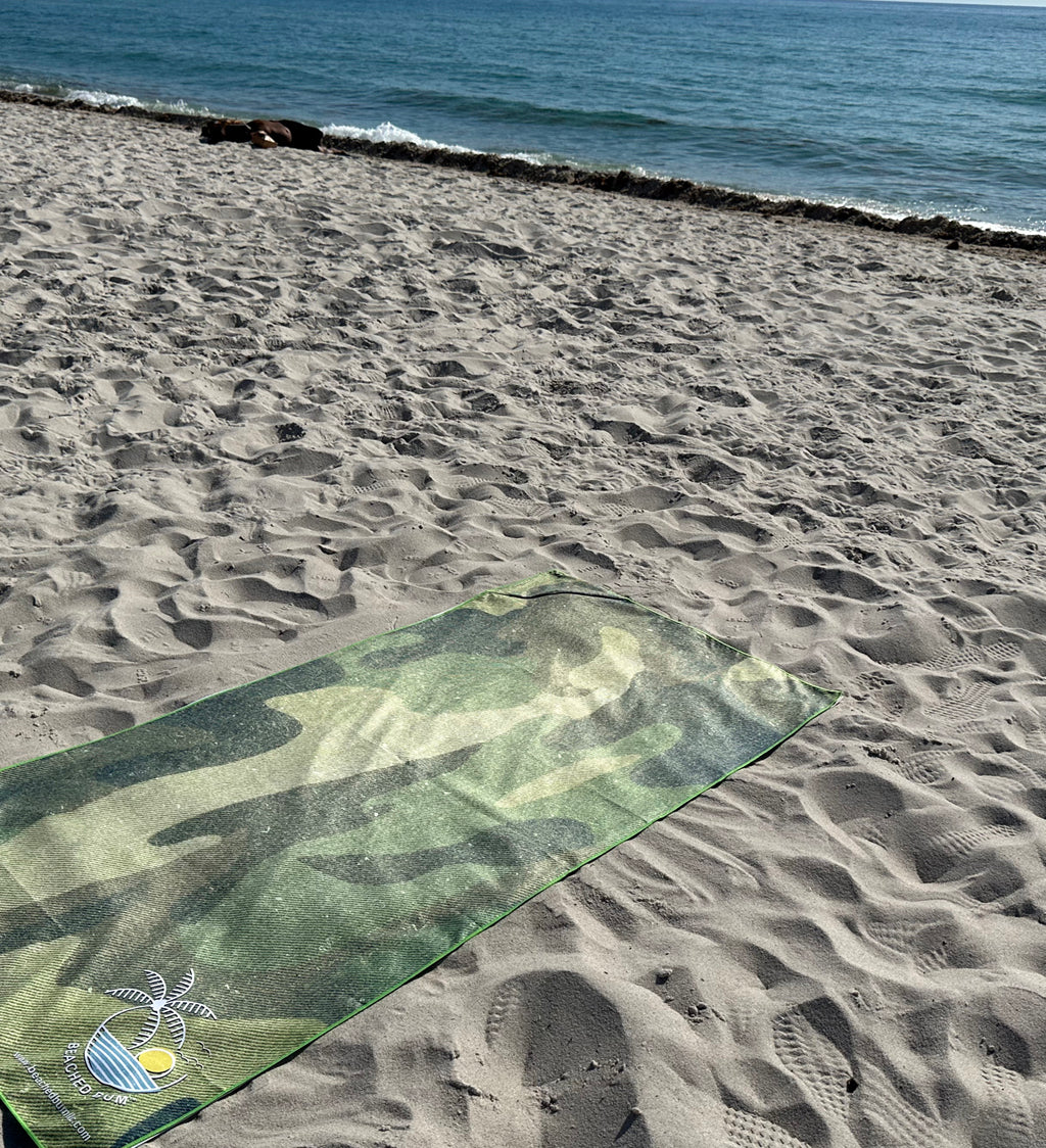 Camouflage-patterned mat on a sandy beach with ocean in the background