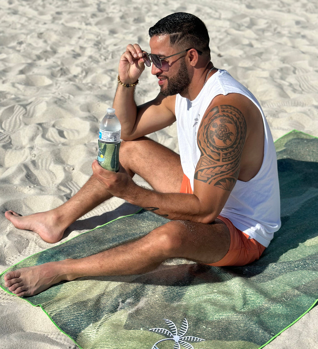 Man sitting on a towel at the beach, holding a water bottle.