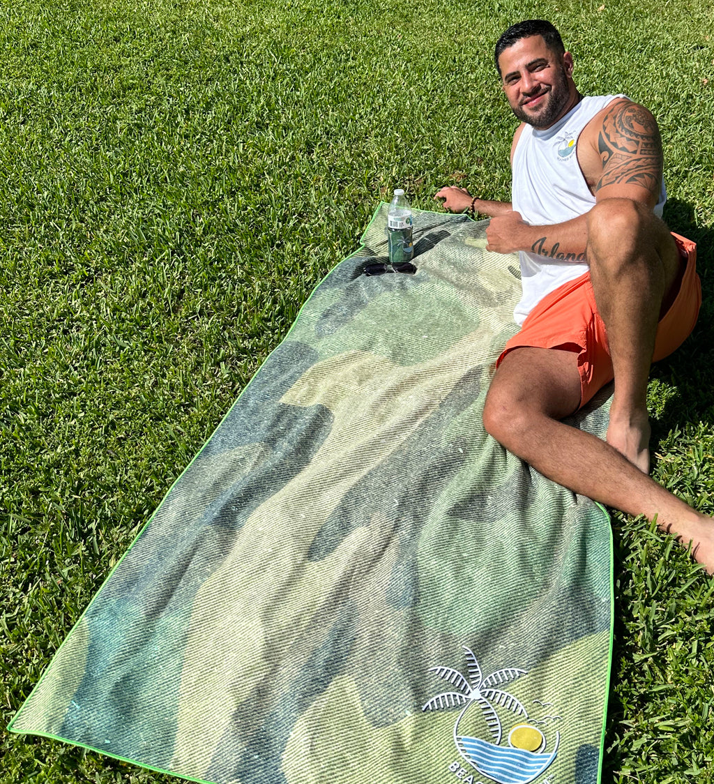 Man sitting on a green towel with a palm tree design on grass