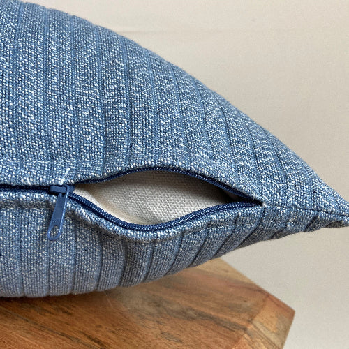 Blue textured pillow on a wooden surface with a neutral background