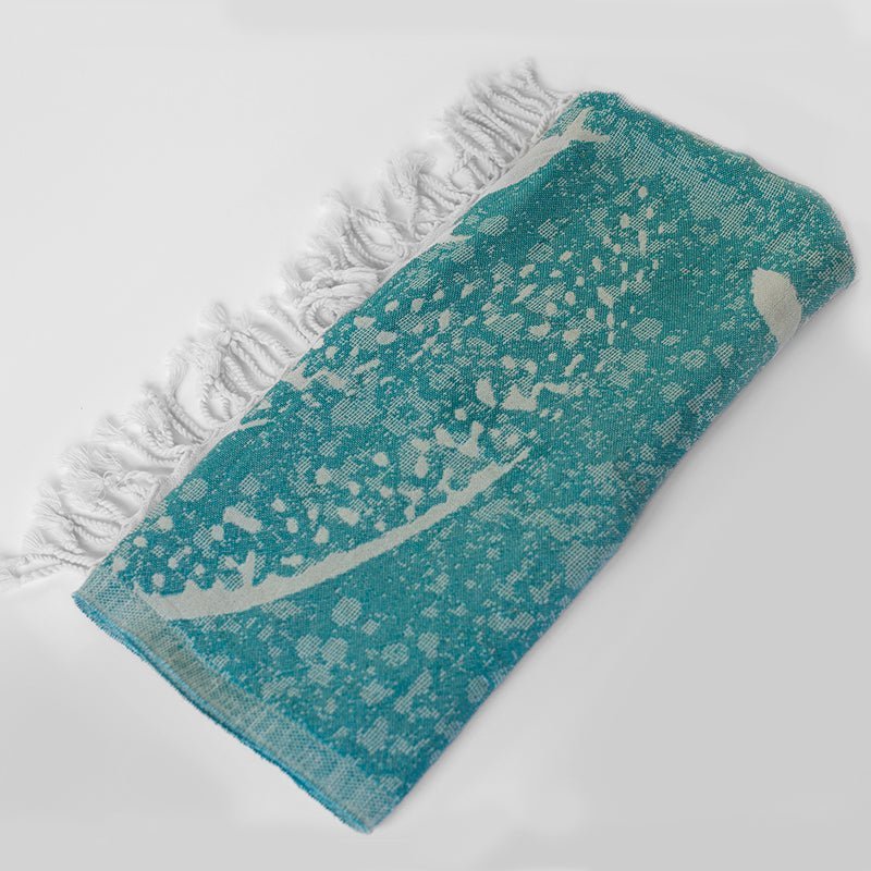 Teal towel with white pattern and fringe on a light gray background