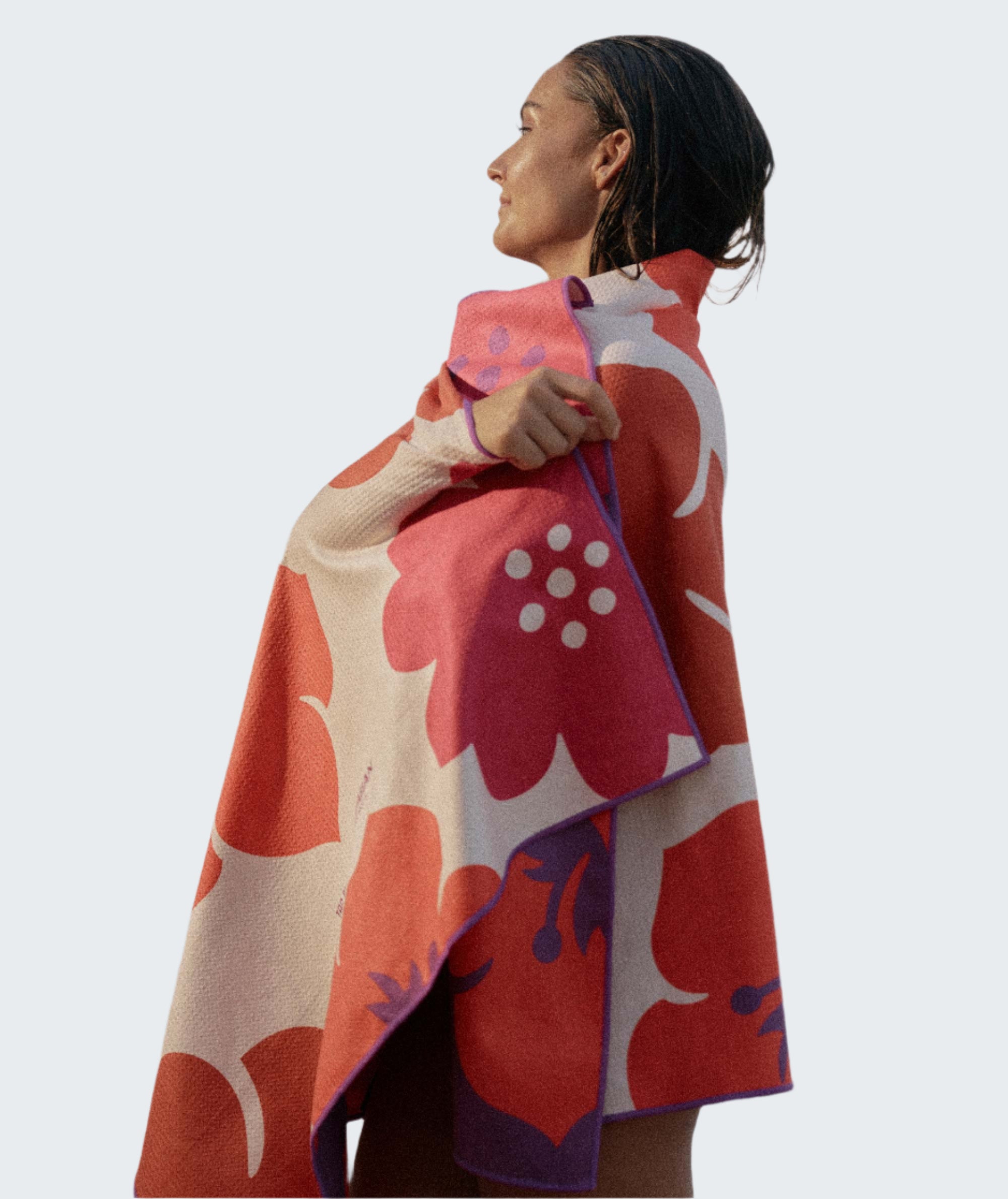 Woman wrapped in a colorful floral-patterned towel on a beach at sunset.