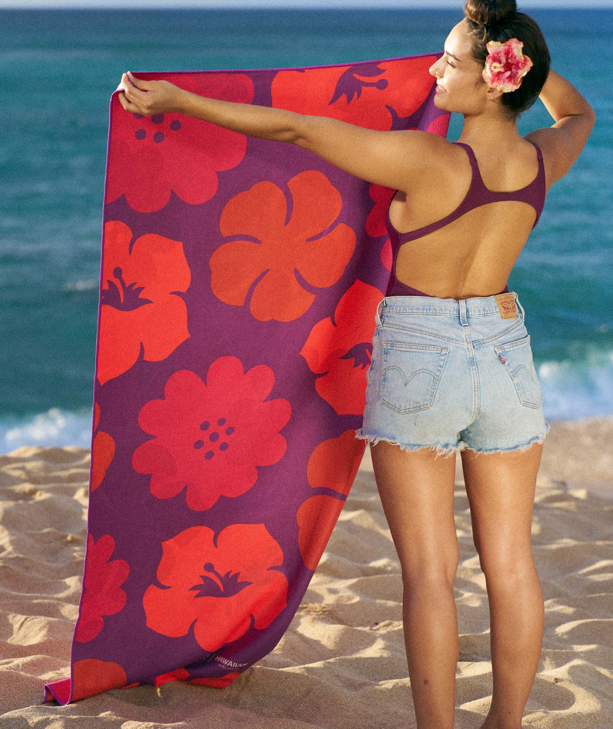 Woman holding a red floral towel on a beach
