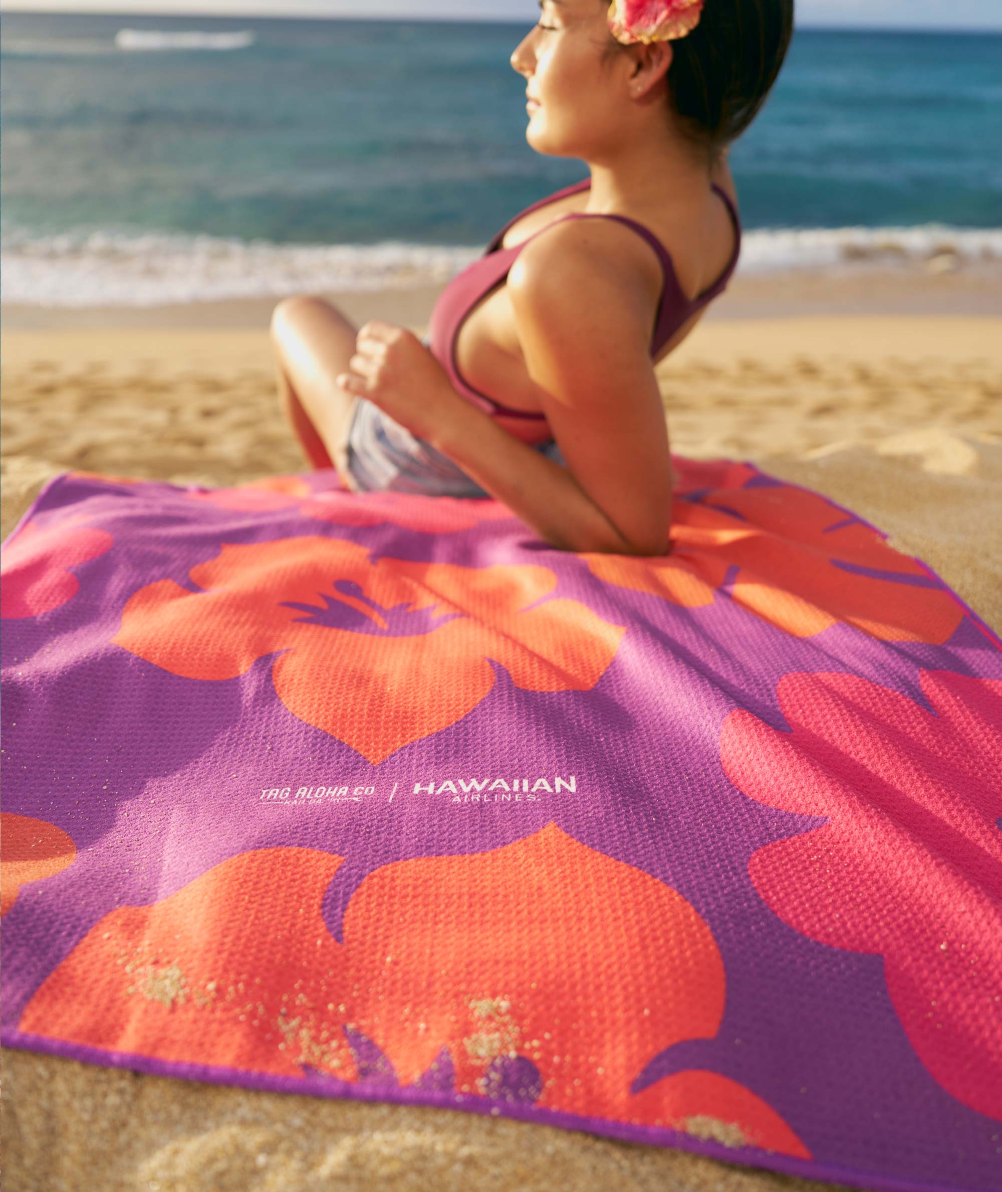 Woman sitting on a colorful beach towel with floral design on a sandy beach.