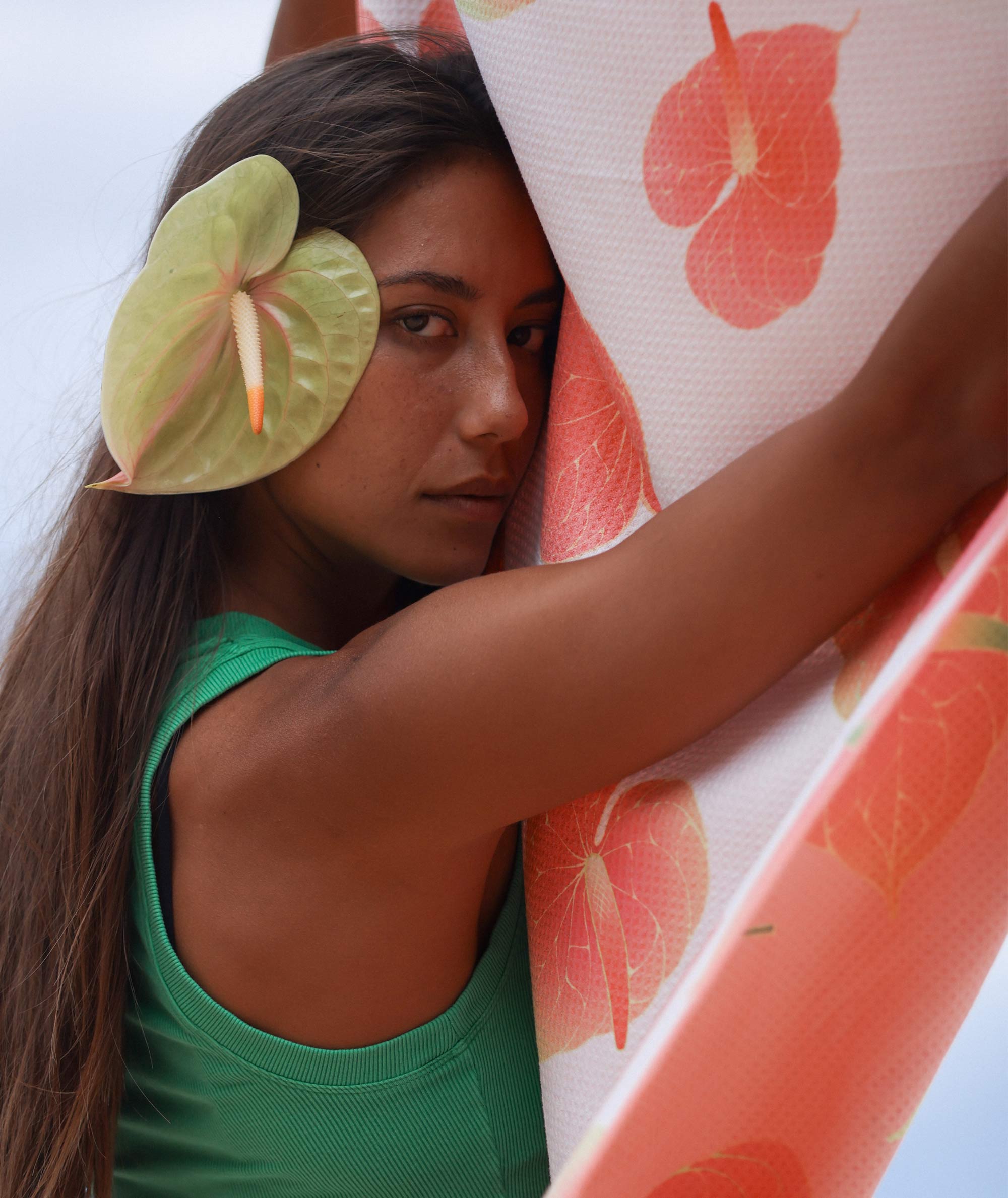 Woman holding a surfboard with a floral design, wearing a green top.