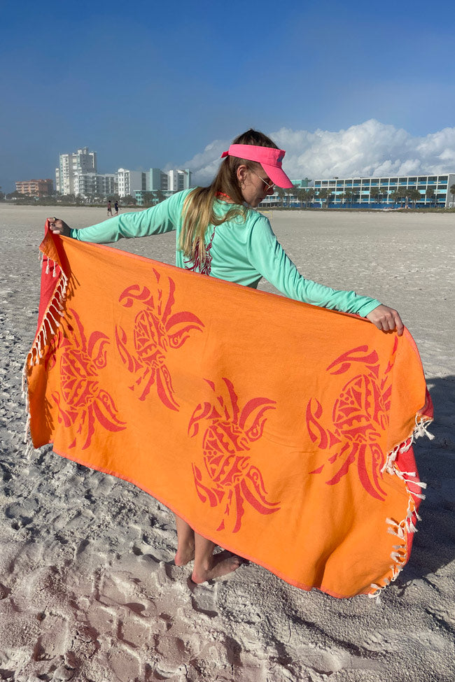 Person holding an orange towel with red patterns on a beach