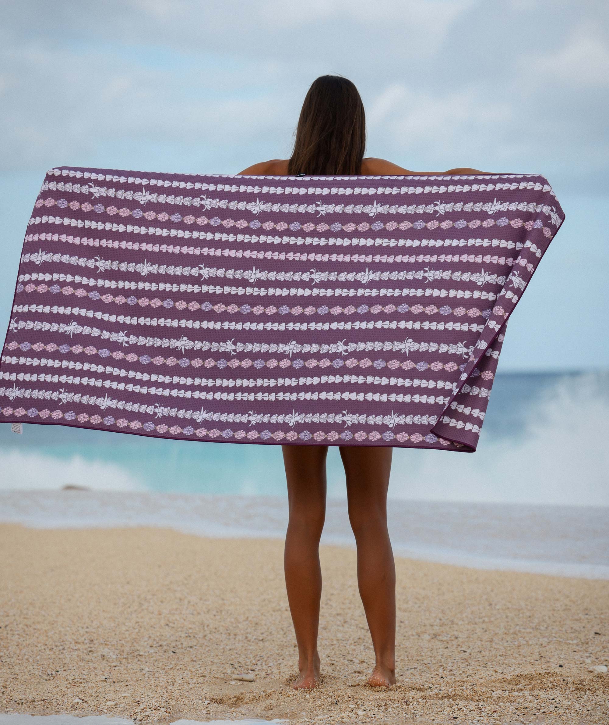 Person holding a purple and white patterned towel on a beach