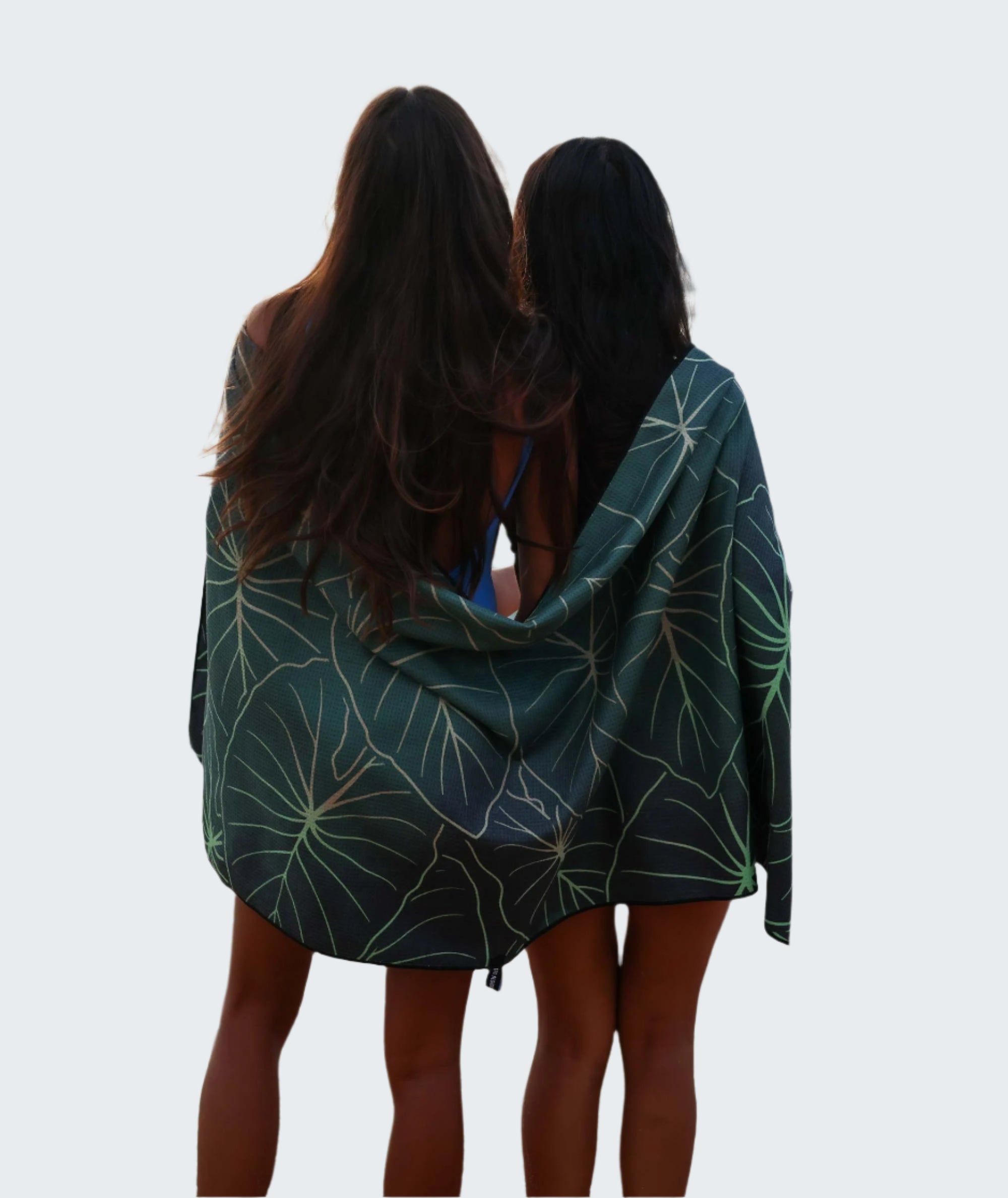 Two people standing on a beach with a green leaf-patterned towel draped over them.