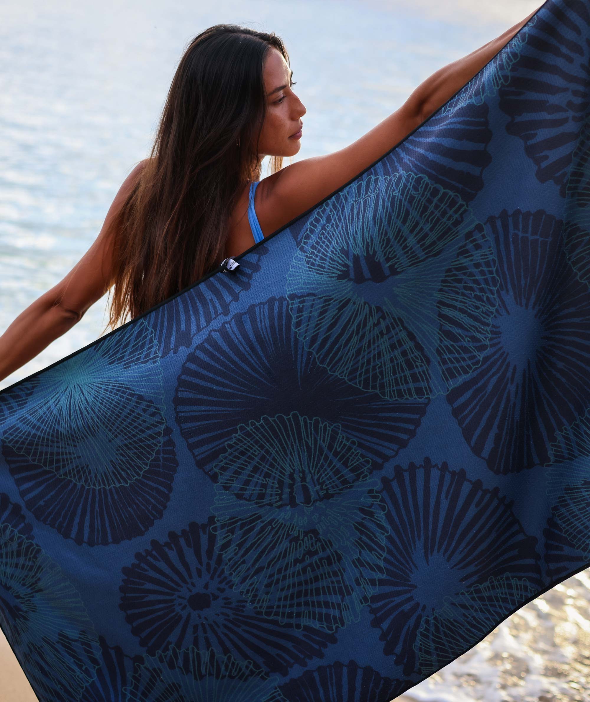 Woman holding a blue patterned towel by a body of water