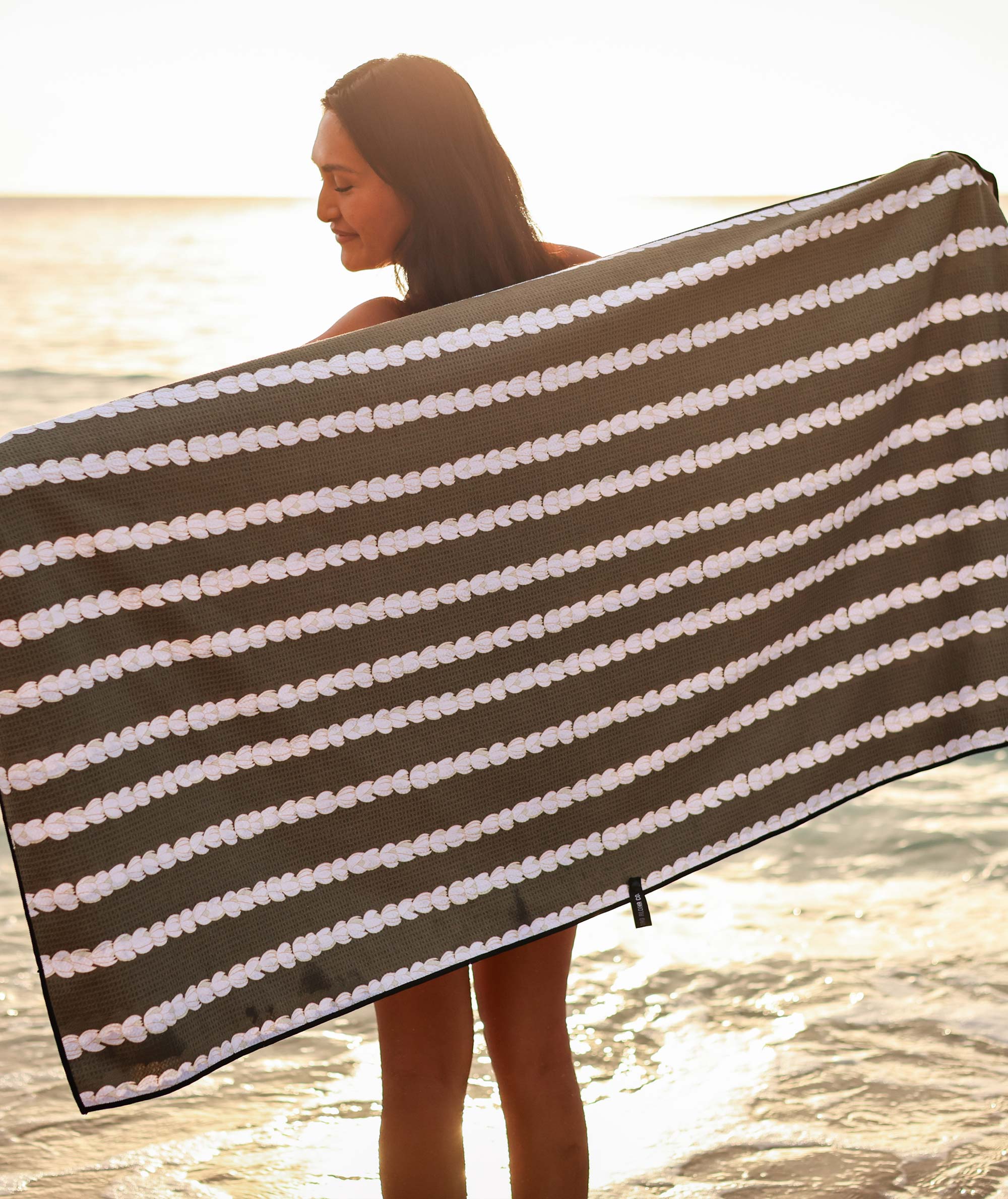 Woman holding a large brown and white striped towel by the beach