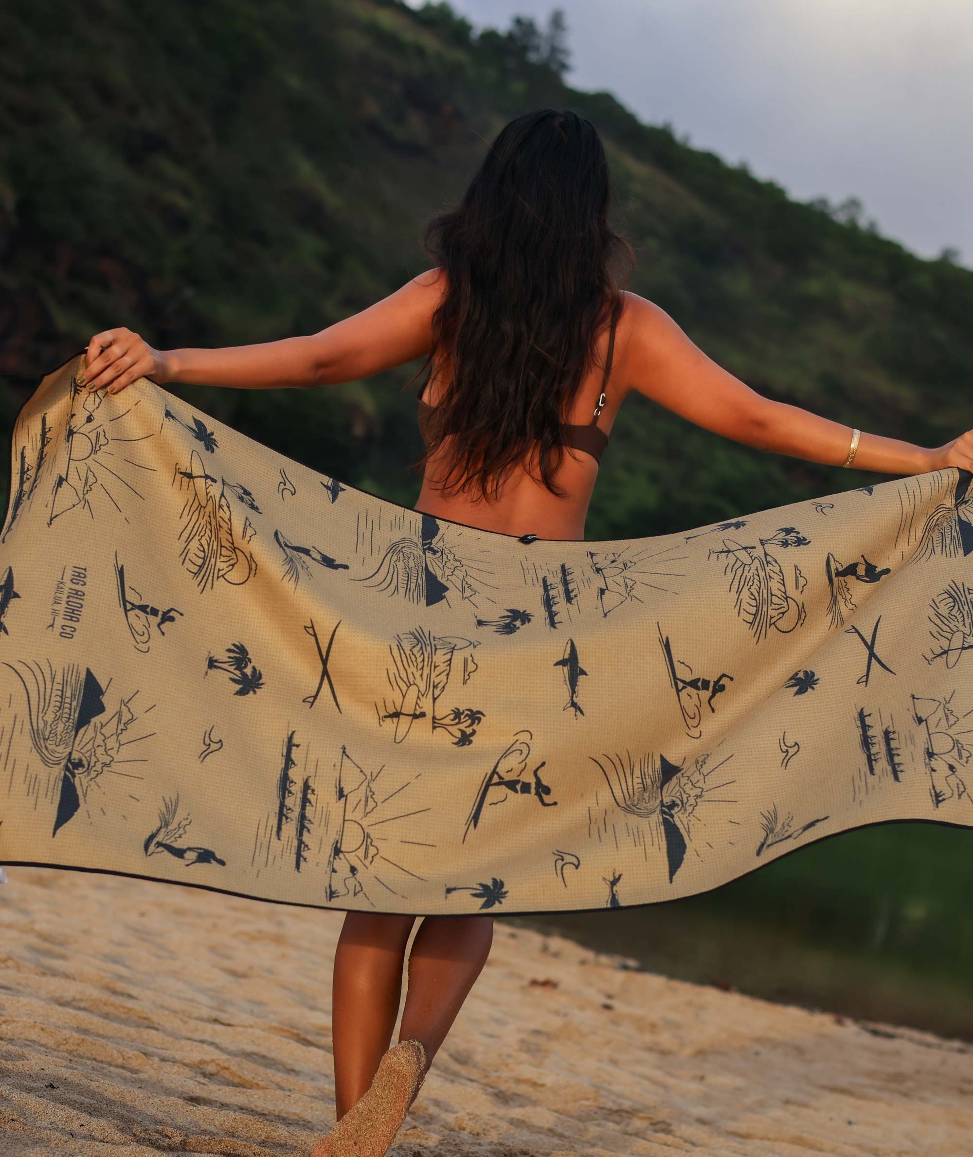 Woman holding a large beach towel with nature patterns on a beach.