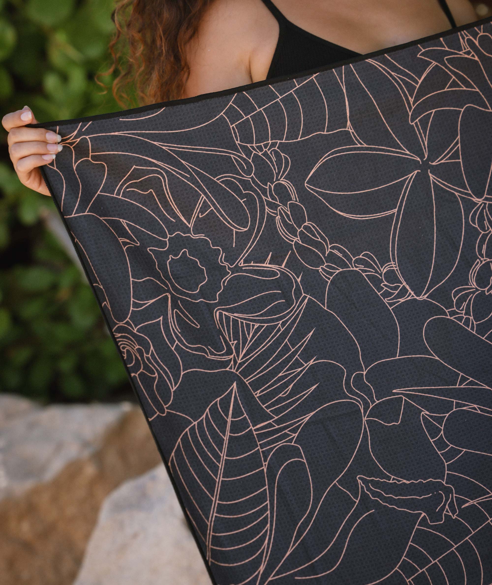 Person holding a black fabric with floral pattern against a natural background