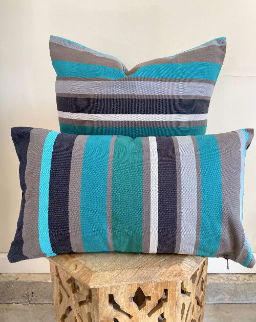 Two striped pillows with blue and gray colors on a wooden stool.