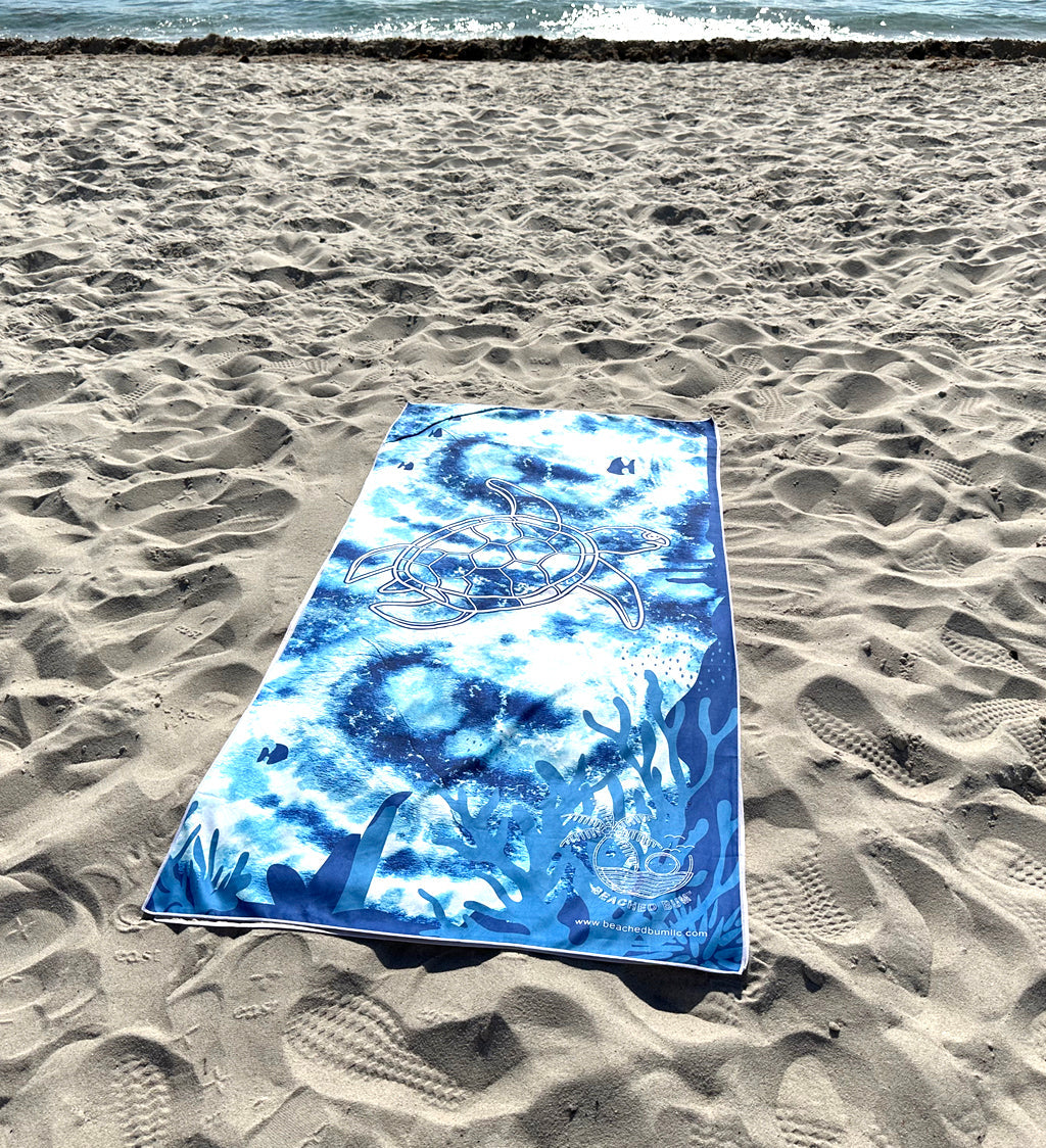 Blue tie-dye towel with ocean design on sandy beach