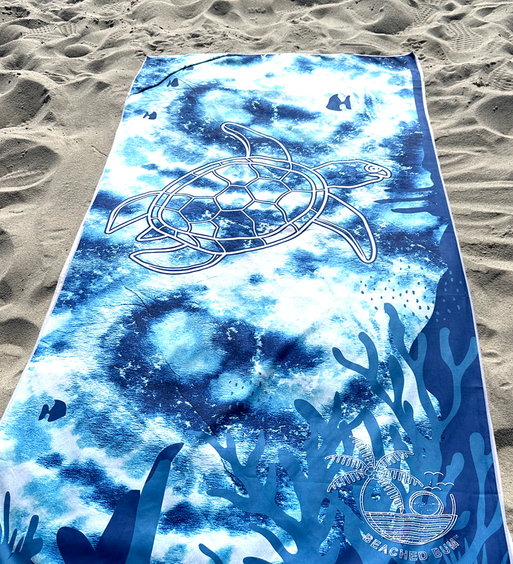 Blue ocean-themed towel with turtle design on sandy beach