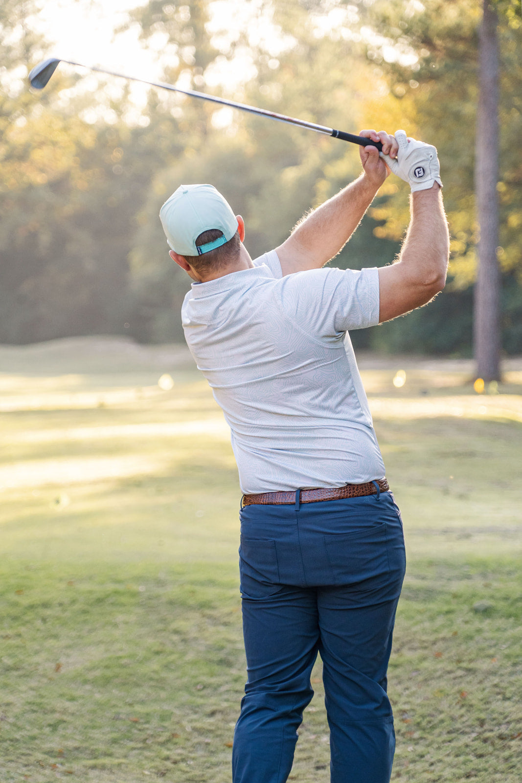 Man playing golf on a grassy field with trees in the background