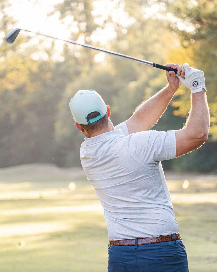 Man playing golf on a sunny day with trees in the background