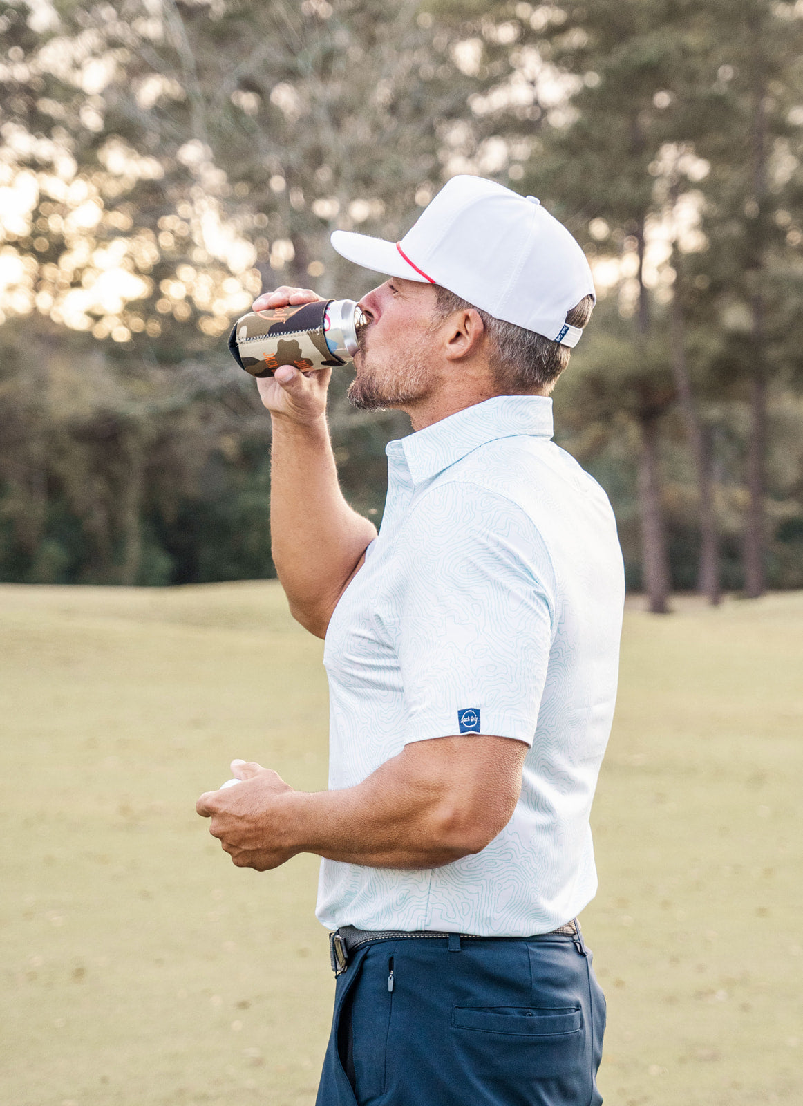 Man in golf attire drinking from a bottle on a golf course