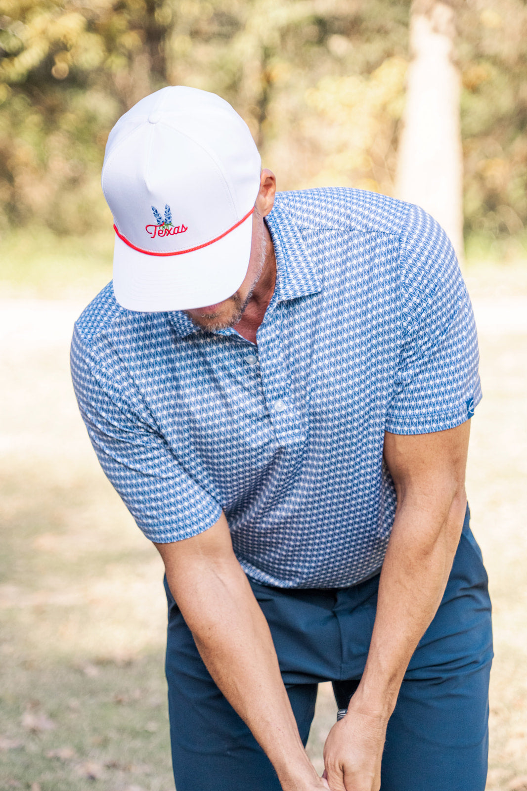 Man in blue checkered shirt and white cap with red logo on a golf course