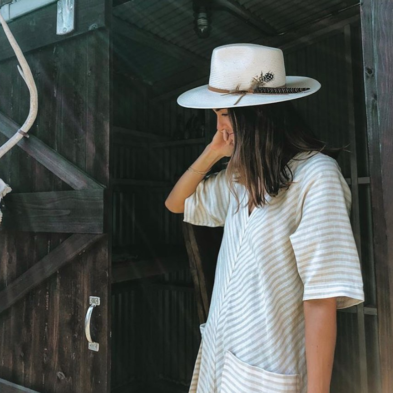 Woman wearing a white hat and striped dress in a rustic setting