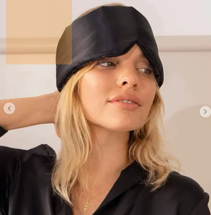 Woman wearing a black satin sleep mask against a neutral background