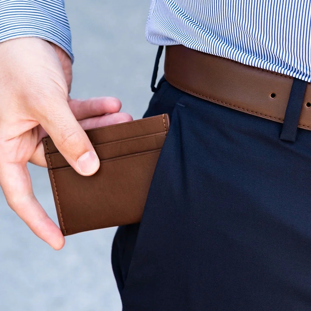 Person holding a brown leather cardholder with a neutral background
