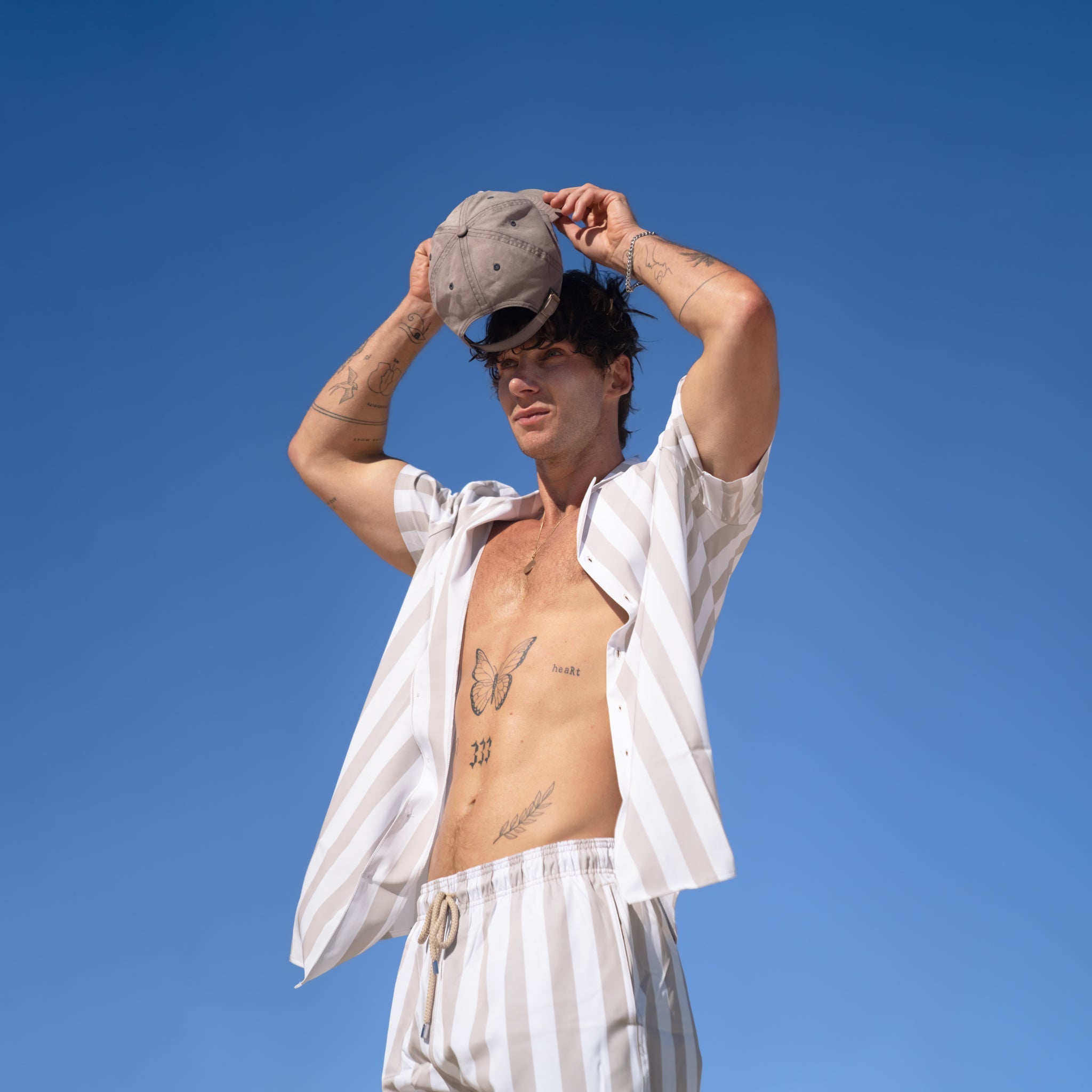 Man in white shirt and shorts holding a cap against a clear blue sky