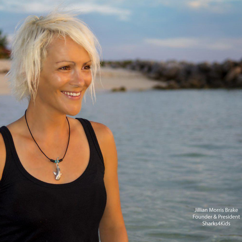 Woman with blonde hair and a black tank top standing by a body of water, with 'Sharks4Kids' branding.