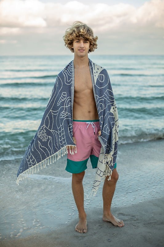 Person standing on a beach with a towel draped over their shoulders